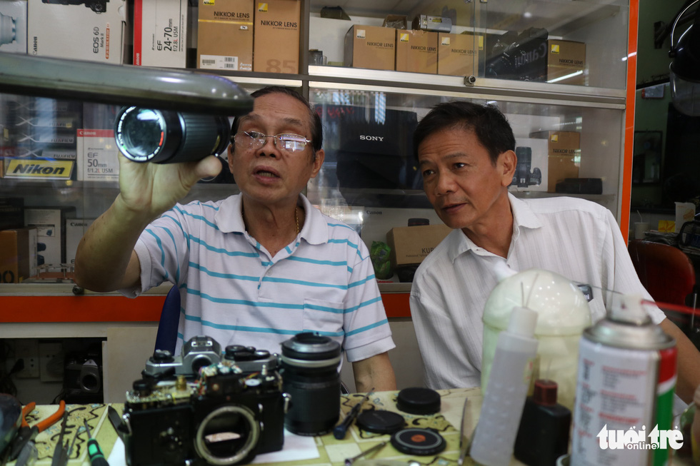 Nguyen Van Tan (left) discusses while repairing a camera for his customer. Photo: Ngoc Phuong/ Tuoi Tre