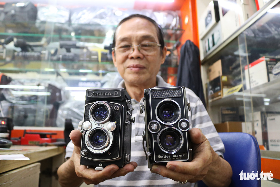 Tan poses with two film cameras at his work. Photo: Ngoc Phuong/ Tuoi Tre