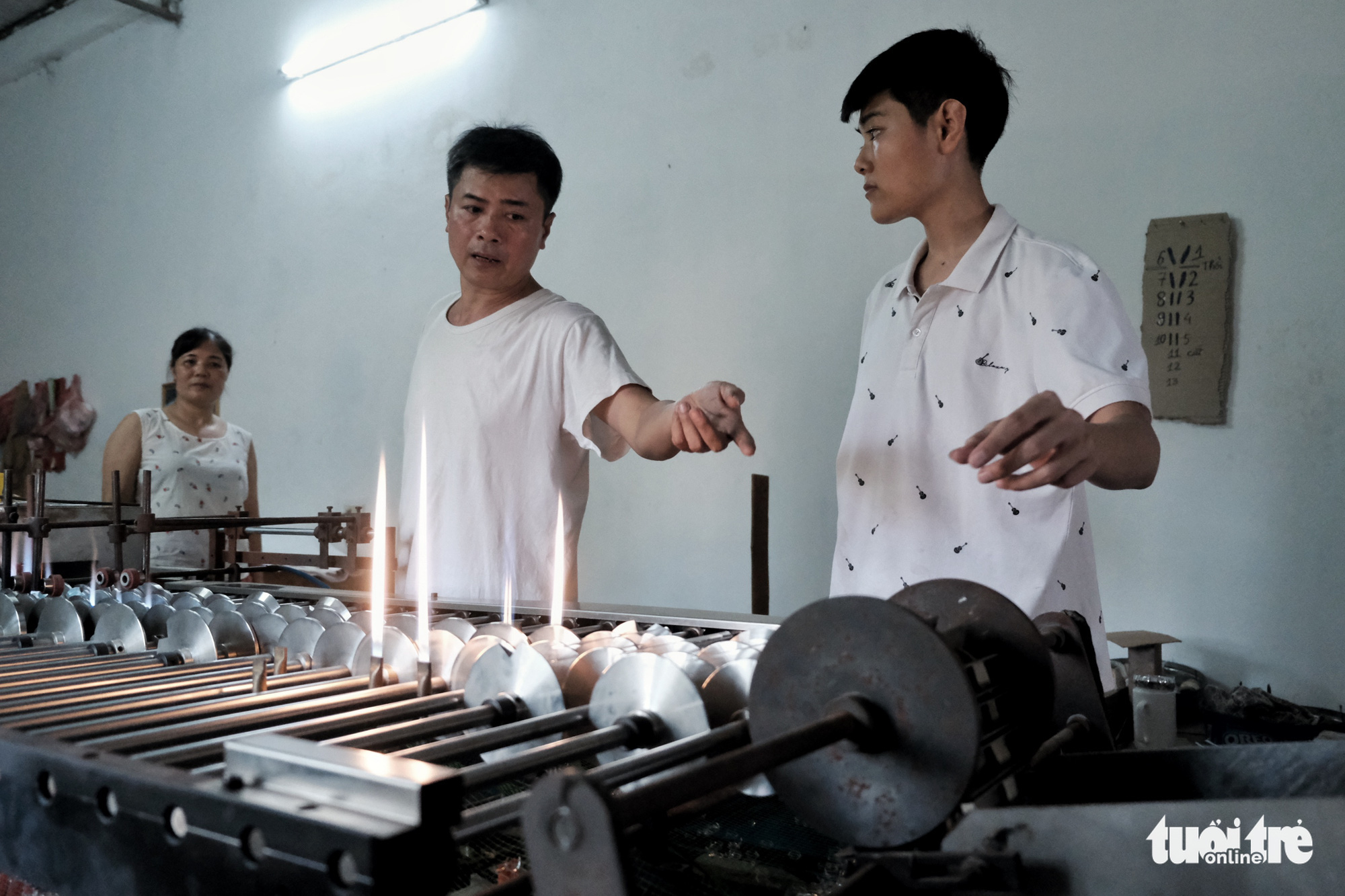 Ta Thi Nga (left), her husband Luong Van Trai (center) and their son are seen operating a machine which churns out test tubes. Photo: Mai Thuong / Tuoi Tre
