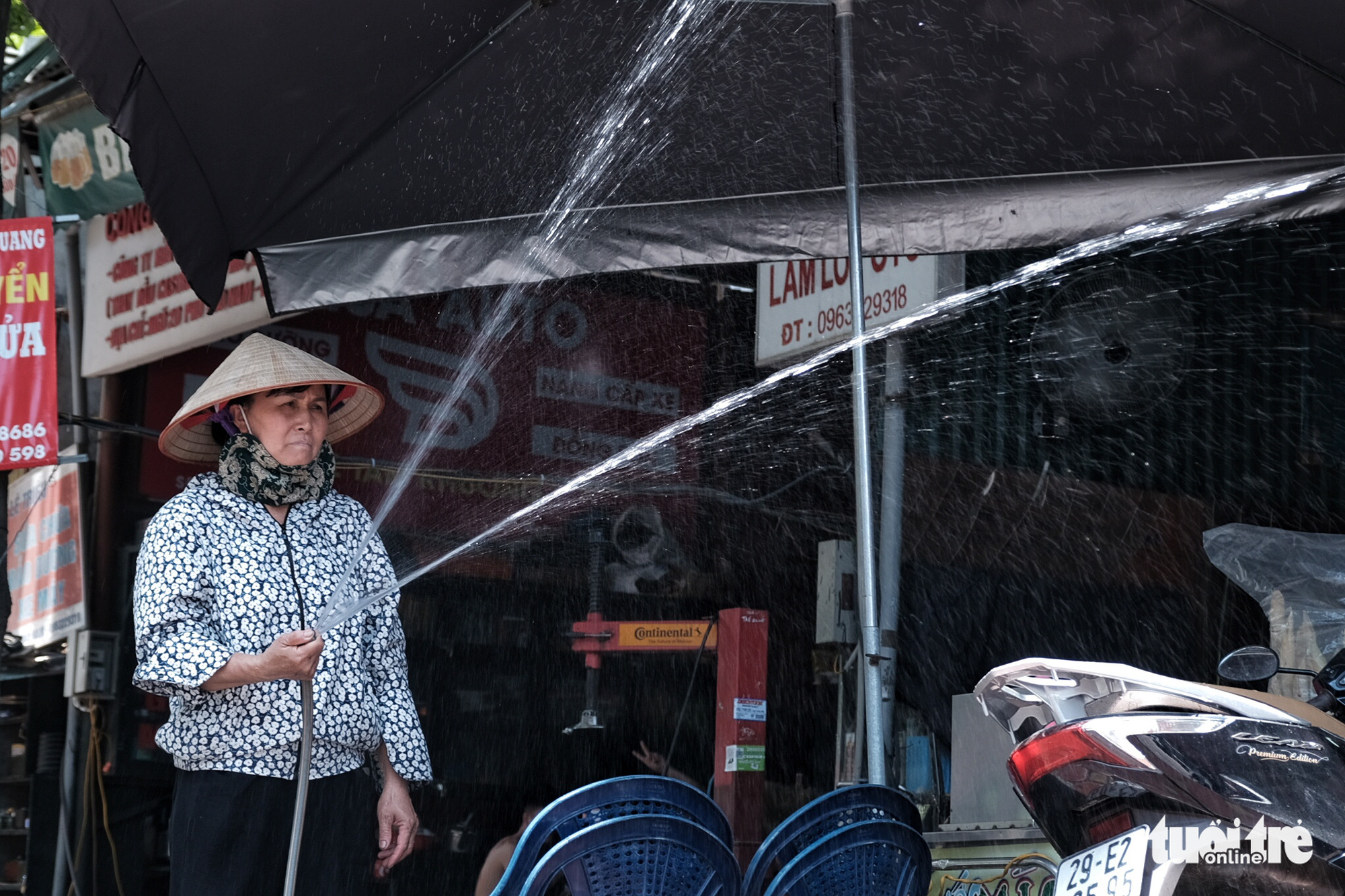 A woman sprays water onto the street to ease the heat in Hanoi, June 23, 2020. Photo: Mai Thuong / Tuoi Tre