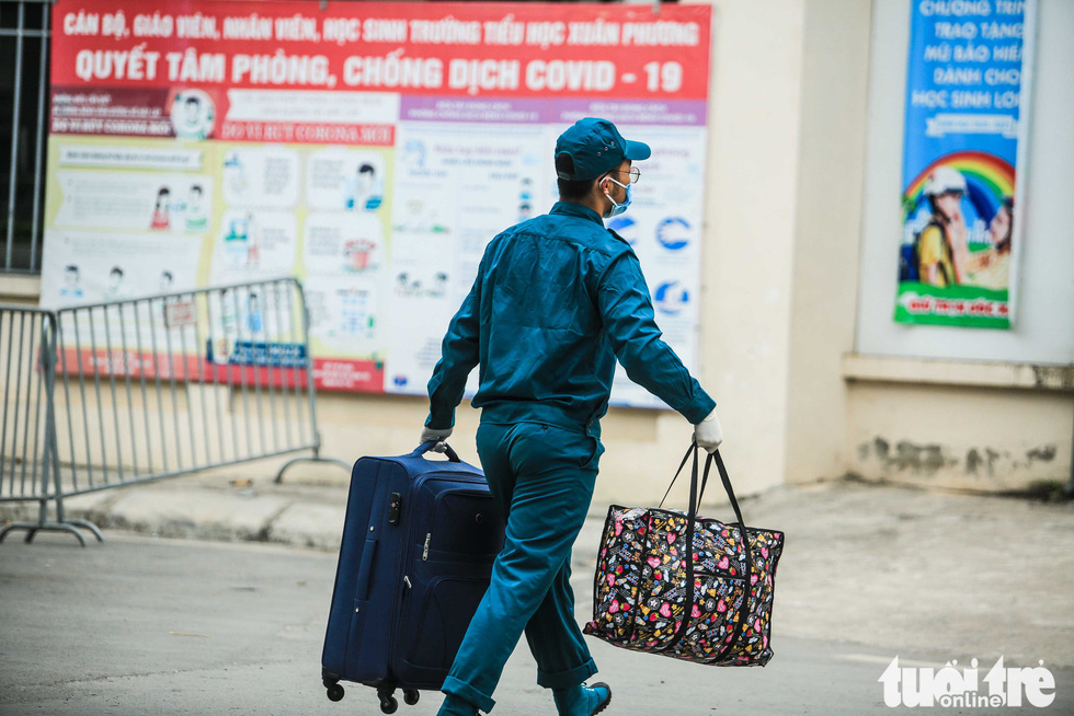 Local guards carry baggage of the quarantined individuals inside Xuan Phuong Primary School, January 31, 2021. Photo: Nguyen Khanh / Tuoi Tre
