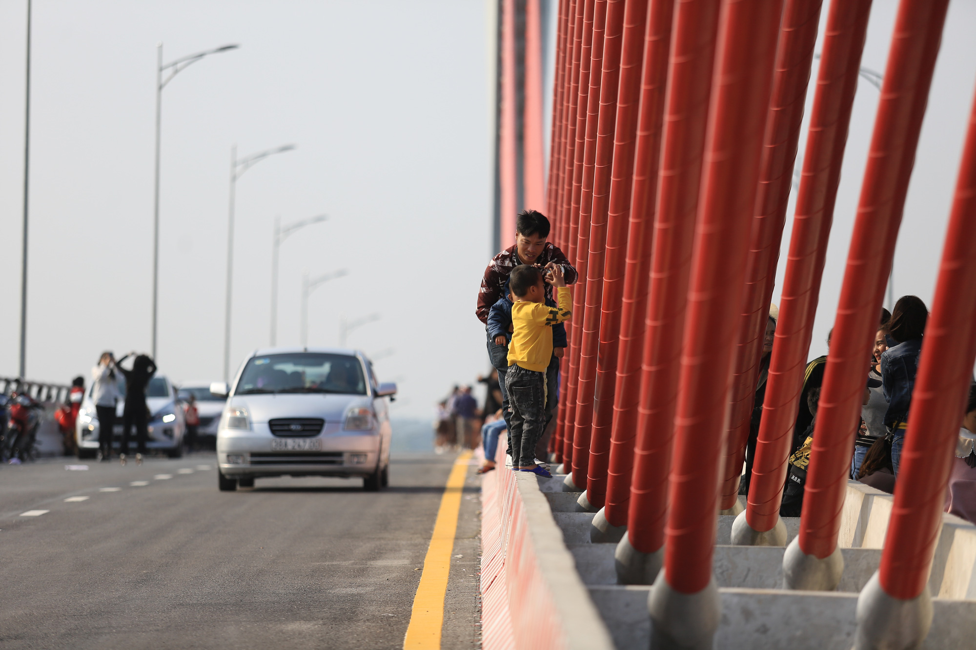 A man allows a child to climb the stayed cable on the Cua Hoi Bridge to take photos in north-central Vietnam, February 15, 2021. Photo: Ngoc Thang / Tuoi Tre